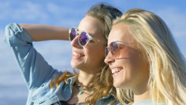 Portrait Shot of Two Beautiful Happy Girls Wearing Sunglasses Embrace, Laugh and Have Lots of Fun. Clear Blue Sky is Seen in the Background. — Stock Video