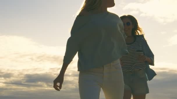 Zwei schöne Mädchen, die sich an den Händen halten und in die wolkenlose glückliche Zukunft rennen. Klarer Himmel im Hintergrund. — Stockvideo