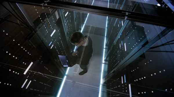 Vista dall'alto attraverso il vetro dell'ingegnere IT che lavora con il computer portatile nel data center pieno di server rack attivi . — Foto Stock