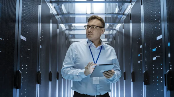 Het technicus doorloopt rijen van Server Racks in datacenter. Tegelijkertijd werkt hij op een Tablet-PC. — Stockfoto