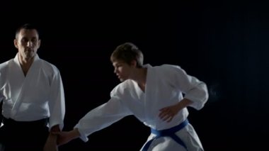 Dövüş sanatları ustası Hakamas giyen genç öğrenci Aikido üzerinde omuz atış atma tekniği siyah arka plan üzerine ve yavaş hareket izole öğretir. 