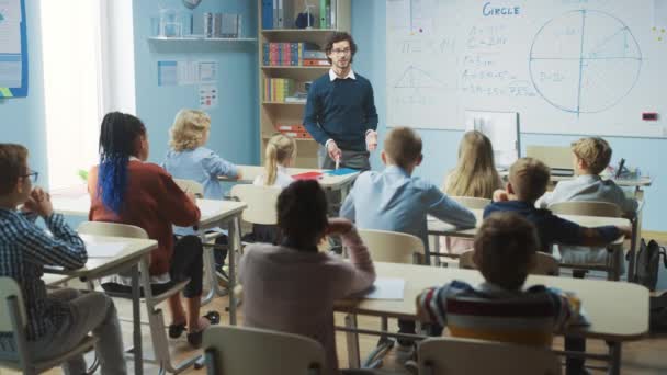 El maestro entusiasta explica lecciones y hace preguntas desde un aula llena de niños brillantes y diversos. En la Escuela Primaria Grupo de Niños Multiétnicos Inteligentes Aprendiendo Ciencia y Pensamiento Creativo — Vídeo de stock