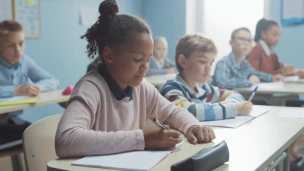 Çeşitli Çocuklar İlköğretim Sınıfı Öğretmenlerinin Ders Vermesini Dikkatle Dinliyor. Egzersiz kitaplarında yazan, Sınav ve Sınavlara giren zeki çocuklar. Öğrenen Çocuklar — Stok video