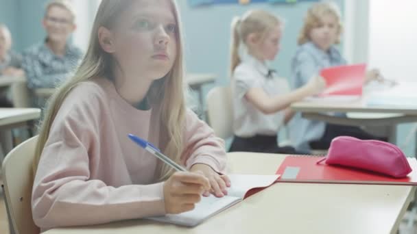 Na escola primária, a menina branca da sala de aula escreve em caderno de exercícios, fazendo teste e exame de escrita. Sala de aula Júnior com Grupo Diverso de Crianças Trabalhando Diligentemente e Aprendendo Novas Coisas — Vídeo de Stock