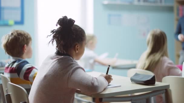 In Elementary School Class: Portret van een briljant zwart meisje met beugels Schrijft in Exercise Notebook, glimlacht. Junior Classroom met diverse groep van heldere kinderen Werken en leren van nieuwe dingen — Stockvideo