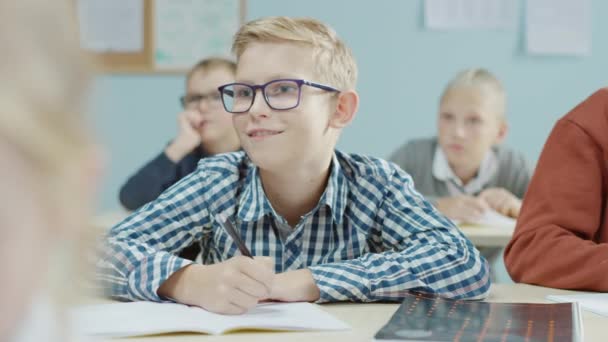 In de basisschoolklas: Portret van een briljante blanke jongen met een bril Schrijft in het oefenschrift. Diverse Groep Heldere Kinderen Leren Wetenschap en Creatief Denken — Stockvideo