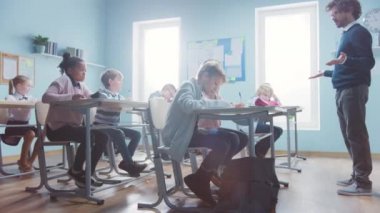 Coşkulu Öğretmen Çeşitli Çocuklarla dolu bir sınıfa Dersi Açıklıyor. Egzersiz Kitapları ve Öğrenme dalında Çok Irklı Çocuklar İlköğretim Okulunda. Yan Görünüm Hareket Görüntüsü