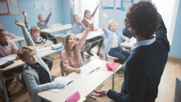 Grundschulklasse mit bunt gemischten Kindern, die zuhören, wie der Lehrer ihnen eine Lektion erteilt. Jeder hebt die Hand und weiß die richtige Antwort. Brillante Kinder in der Schule lernen. Lehrer über Schulter erschossen — Stockvideo