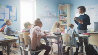 Coşkulu Öğretmen, Çeşitli Parlak Çocuklarla dolu bir sınıfa Ders Açıklarken Dijital Tablet Bilgisayar kullanıyor. Çok Irklı Çocuklar İlköğretim Okulu Öğrenme Grubu 'nda.