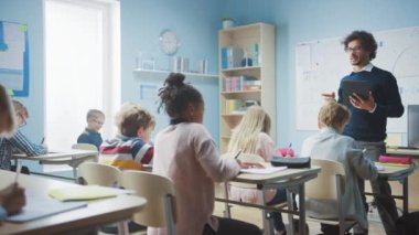 Coşkulu Öğretmen, Çeşitli Parlak Çocuklarla dolu bir sınıfa Ders Açıklarken Dijital Tablet Bilgisayar kullanıyor. Çok Irklı Çocuklar İlköğretim Okulu Öğrenme Grubu 'nda.