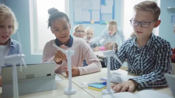 In der Grundschule: Eine Klasse intelligenter Kleinkinder arbeitet im Team mit Tablet-Computern, um Windräder zu programmieren. Unterricht mit Kindern über umweltfreundliche Formen erneuerbarer Energien — Stockvideo