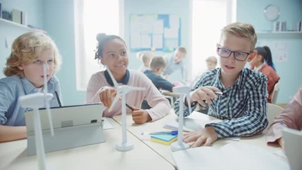 In de basisschool: klasse van slimme jonge kinderen werken als een team met behulp van tabletcomputers om windturbines te programmeren. Klaslokaal met kinderen die leren over milieuvriendelijke vormen van hernieuwbare energie — Stockvideo