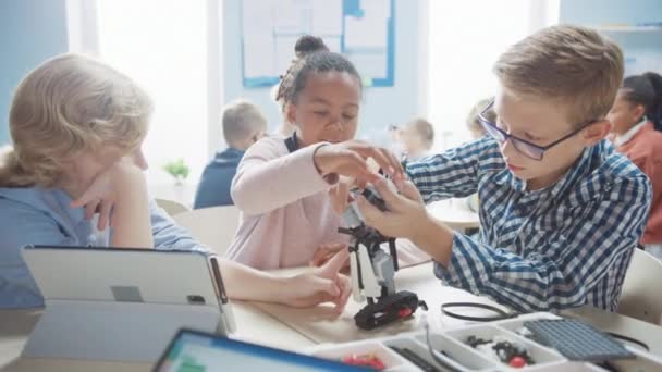 Elementary School Robotics Classroom: Diverse Group of Brilliant Children Building and Programming Robot, Talking and Working as a Team. Crianças aprendendo design de software e engenharia de robôs criativos — Vídeo de Stock