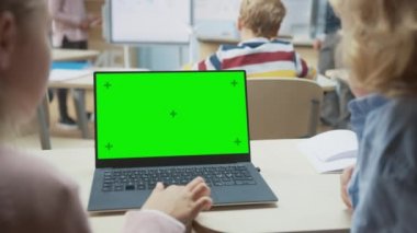 İlköğretim Okulu Sınıfı: Sınıfta Yeşil Laptop Kullanan İki Çocuğun Omuz Görünümü Üzerine. Arka plan Öğretmeninde Çeşitli Sınıflara Ders Açıklanıyor