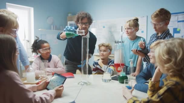 Clases de Ciencia / Química en la Escuela Primaria: El Profesor Muestra Experimento de Reacción Química al Grupo de Niños. Mezcla de productos químicos en el vaso de precipitados para obtener la reacción. Los niños usan computadoras de tableta digital — Vídeo de stock