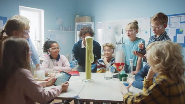 Elementary School Science / Chemistry Classroom: Enthusiastic Teacher Shows Funny Chemical Reaction Experiment to Group of Children Змішуючи хімікати в бейкері, вони стріляють в піну (зубна паста слона).) — стокове відео