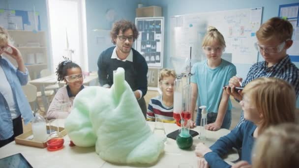 İlköğretim Okulu Bilim / Kimya Sınıfı: Coşkulu Öğretmen Çocuklar Grubu 'na Komik Kimyasal Tepkime Deneyi Gösteriyor. Beher 'de kimyasalları karıştırıp köpük atıyorlar (Fil diş macunu) — Stok video