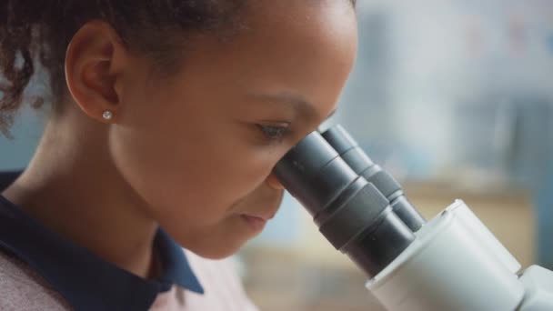 Porträtt av Smart Little Schoolgirl Looking Under the Microscope. I grundskolan klassrum söt flicka använder mikroskop. STEM (naturvetenskap, teknik, teknik och matematik) Utbildningsprogram — Stockvideo
