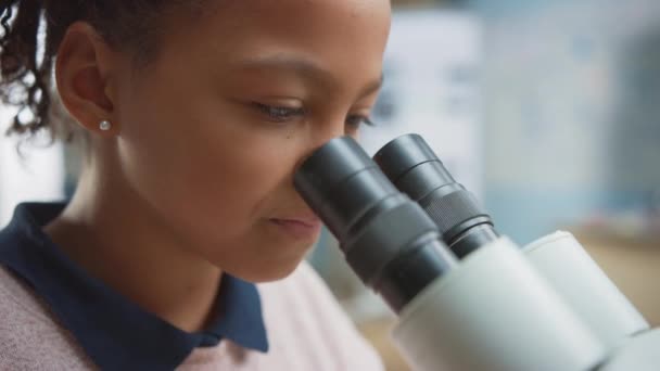 Porträtt av Smart Little Schoolgirl Looking Under the Microscope. I grundskolan klassrum söt flicka använder mikroskop. STEM (naturvetenskap, teknik, teknik och matematik) Utbildningsprogram — Stockvideo