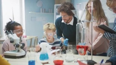 İlköğretim Okulu Bilim Sınıfı: Coşkulu Öğretmen Kimyayı Farklı Çocuklar Grubu 'na Açıklıyor, Kimyasalları Şişelerde Nasıl Karıştıracaklarını Gösteriyor. Çocuklar Dijital Tablet Bilgisayarları Kullanır ve Konuşur