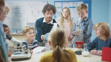 İlköğretim Okulu Bilim Sınıfı: Coşkulu Öğretmen Kimyayı Farklı Çocuklar Grubu 'na Açıklıyor, Kimyasalları Şişelerde Nasıl Karıştıracaklarını Gösteriyor. Çocuklar Dijital Tablet Bilgisayarları Kullanır ve Konuşur