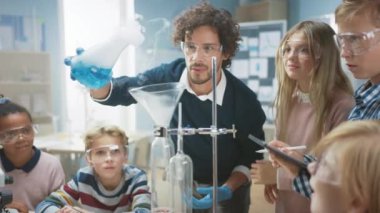 İlköğretim Okulu Bilim Sınıfı: Coşkulu Öğretmen Kimyayı Farklı Çocuklar Grubu 'na Açıklıyor, Kimyasalları Şişelerde Nasıl Karıştıracaklarını Gösteriyor. Çocuklar Dijital Tablet Bilgisayarları Kullanır ve Konuşur