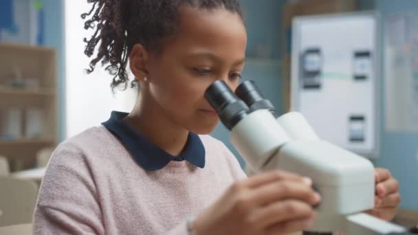 Porträtt av Smart Little Schoolgirl Looking Under the Microscope. I grundskolan klassrum söt flicka använder mikroskop. STEM (naturvetenskap, teknik, teknik och matematik) Utbildningsprogram — Stockvideo