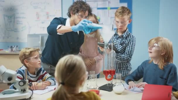 Δημοτικό Σχολείο Science Classroom: Ενθουσιαστικός Δάσκαλος Εξηγεί Χημεία σε Ποικίλες Ομάδα των παιδιών, Τους Δείχνει Πώς να Αναμίξετε Χημικά σε Μπίκερς. Τα παιδιά χρησιμοποιούν ψηφιακούς υπολογιστές tablet και ομιλία — Αρχείο Βίντεο