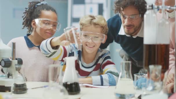 Aula de Ciencias de la Escuela Primaria: Profesor Entusiasta Explica Química a Diverso Grupo de Niños, Niño Pequeño Mezcla Químicos en Beakers. Niños aprenden con interés — Vídeos de Stock