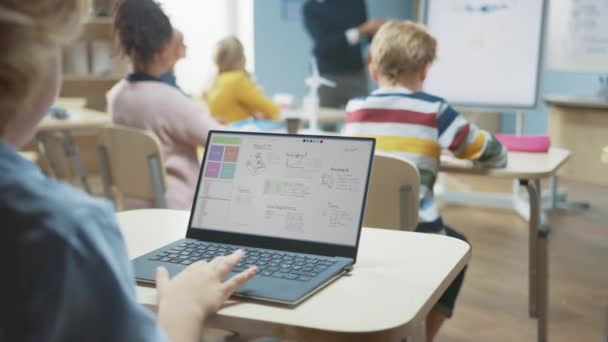 Elementary School Science Class: Over the Shoulder Little Boy utiliza el ordenador portátil con pantalla que muestra el software de programación de robótica de red neuronal. Profesor de Ciencias de la Computación explica lección al aula — Vídeos de Stock