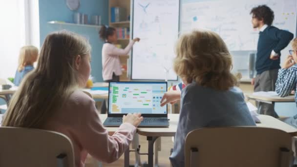 Základní škola Science Class: Přes rameno Little Boy and Girl Use Laptop with Screen Show Programming Software. Učitel fyziky vysvětluje lekci z různorodé třídy plné chytrých dětí — Stock video