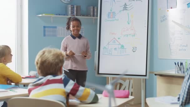 Grundskola Science Class: Söt flicka använder interaktiv digital whiteboard för att visa ett klassrum fullt av klasskamrater hur förnybar energi fungerar. Vetenskap klass, nyfikna barn lyssna — Stockvideo