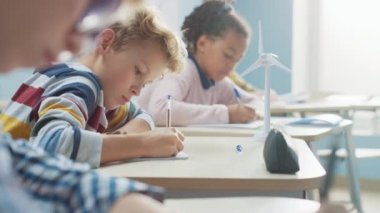 İlköğretim Okulu 'nda parlak beyaz çocuk egzersiz defterinde yazıyor, sınava giriyor ve yazı sınavına giriyor. Bir grup çocuğun özenle çalıştığı ve yeni şeyler öğrendiği küçük sınıf.