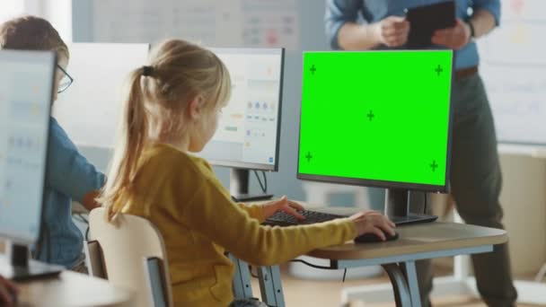 Початкова школа комп'ютерних наук Класна кімната: мила маленька дівчинка використовує зелений макет екрану комп'ютера під час навчання кодування та програмування. Школярі отримують сучасну освіту. Над плечем — стокове відео