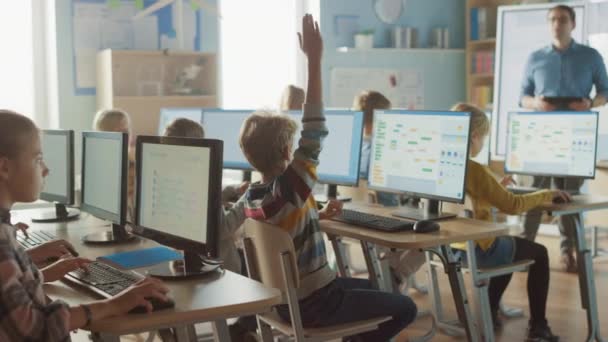 Δημοτικό Σχολείο Science Classroom: Δάσκαλος Εκπαιδεύει Smart Little Schoolchildren που εργάζονται σε προσωπικούς υπολογιστές, Μάθετε Γλώσσα Προγραμματισμού για Κωδικοποίηση Λογισμικού. Αγόρι σηκώνει το χέρι με μια ερώτηση — Αρχείο Βίντεο