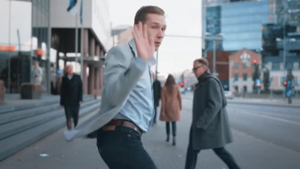 Joyeux jeune homme d'affaires dans un Grey Blazer danse activement sur une rue de la ville. Le gestionnaire de bureau se déplace à travers des foules de bureau occupées pour se rendre au travail. Centre-ville avec des gratte-ciel en arrière-plan . — Video
