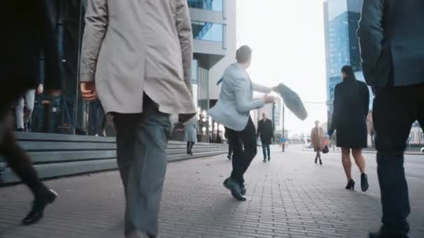 Wesoły młody biznesmen w szarej marynarce aktywnie tańczy na ulicy City. Menedżer biura porusza się przez zajęty tłumy biurowe dojazdy do pracy. Trzyma skórzaną walizkę.. — Wideo stockowe