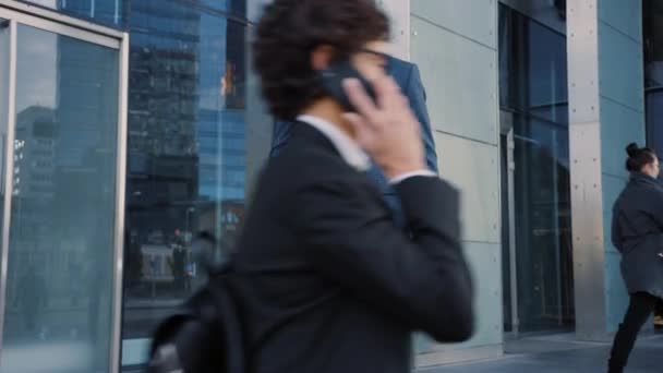 Un hombre de negocios caucásico con traje está usando un teléfono inteligente en una calle en el centro. Otras personas de la oficina caminan más allá. Es confiado y parece exitoso. Está navegando por la web en su dispositivo . — Vídeos de Stock