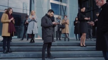 Ofis Yöneticileri ve İş Adamları Modern Cam Ofis Binasının Önünde Duruyorlar ve Akıllı Telefonlarını Kullan. İnsanlar çok şık giyinmiş ve başarılı gözüküyorlar. Aygıtları tarafından işgal ediliyorlar..