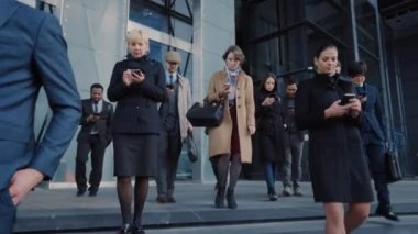 Ofis Yöneticileri ve İş Adamları Modern Cam Ofis Binasının Önünde Yürüyor ve Akıllı Telefonlarını Kullanıyor. İnsanlar çok şık giyinmiş ve başarılı gözüküyorlar. Aygıtları tarafından işgal ediliyorlar..