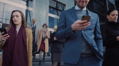 Ofis Yöneticileri ve İş Adamları Modern Cam Ofis Binasının Önünde Yürüyor ve Akıllı Telefonlarını Kullanıyor. İnsanlar çok şık giyinmiş ve başarılı gözüküyorlar. Aygıtları tarafından işgal ediliyorlar..