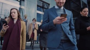 Ofis Yöneticileri ve İş Adamları Modern Cam Ofis Binasının Önünde Yürüyor ve Akıllı Telefonlarını Kullanıyor. İnsanlar çok şık giyinmiş ve başarılı gözüküyorlar. Aygıtları tarafından işgal ediliyorlar..