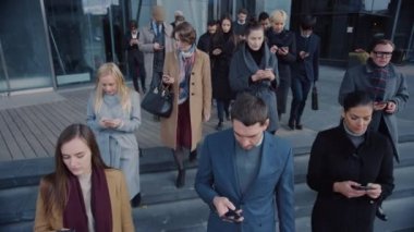 Ofis Yöneticileri ve İş Adamları Modern Cam Ofis Binasının Önünde Yürüyor ve Akıllı Telefonlarını Kullanıyor. İnsanlar çok şık giyinmiş ve başarılı gözüküyorlar. Aygıtları tarafından işgal ediliyorlar..