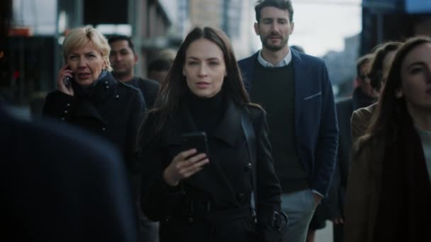 Bella donna d'affari in cappotto nero sta utilizzando uno smartphone su una strada nel centro della città. Cammina su una strada pedonale affollata e sembra di successo. Sta navigando sul Web sul suo dispositivo . — Video Stock