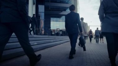 Sokakta yürüyen takım elbiseli bir iş adamı. Diğer ofis çalışanları işe ya da eve gidip geliyor. Sabahın erken saatleri ya da akşamın geç saatleri. Arkadan görüntüler. Şehir Işıkları Arkaplanda.