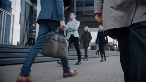 Beinschuss eines Geschäftsmannes in einem Anzug, der zu Fuß ins Büro pendelt. Er trägt eine Ledertasche. Andere Manager und Geschäftsleute gehen in der Nähe. Bewölkter Tag auf einer Straße in der Innenstadt. — Stockvideo