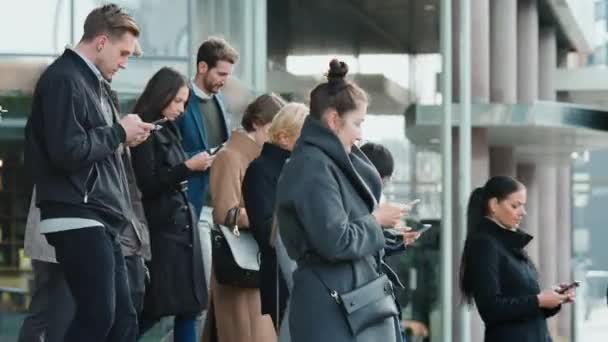 Gerentes de Escritório e Empresários estão caminhando na frente de um prédio de escritórios de vidro moderno e usam seus smartphones. As pessoas estão vestidas de forma inteligente e olhar bem sucedido. Eles são ocupados por seus dispositivos . — Vídeo de Stock