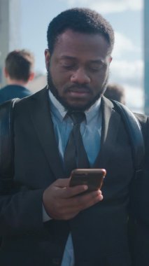 Sokakta yayalarla dikilen takım elbiseli Afrikalı Amerikalı bir iş adamının portresi. O bir Smartphone kullanıyor. Başarılı birine benziyor. Dikey Ekran Yönelimli Video Görüntüsü 9: 16.
