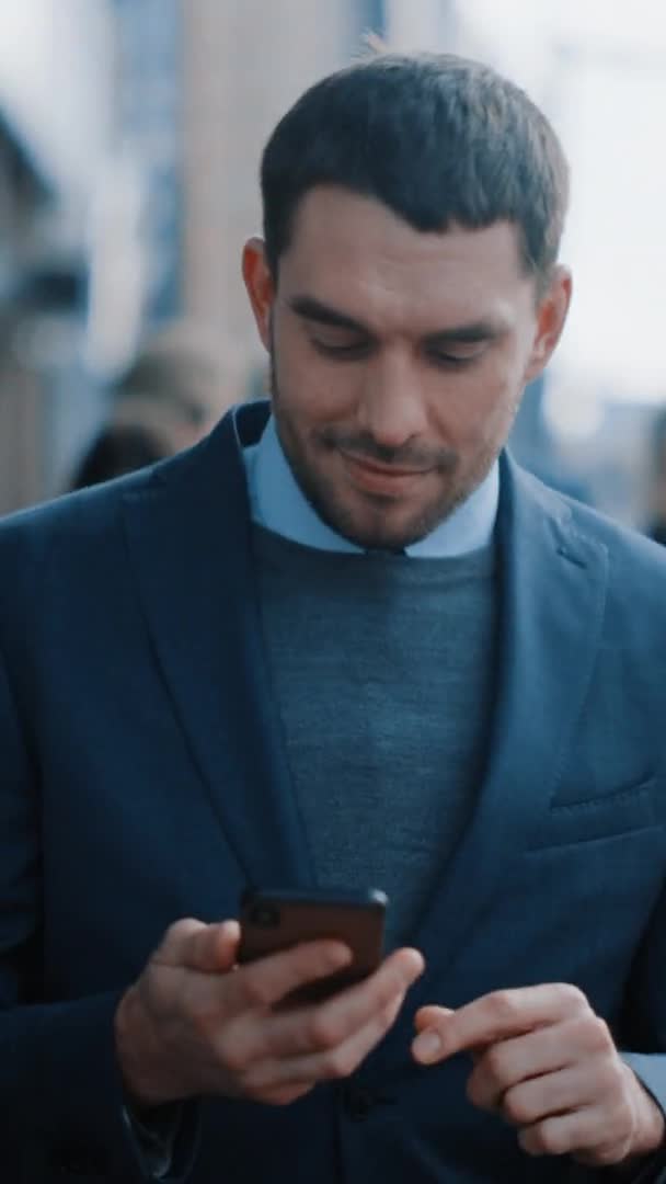 L'uomo d'affari caucasico in giacca e cravatta sta usando uno smartphone in Dark Street la sera. Altre persone dell'ufficio camminano oltre. Filmati video con orientamento verticale dello schermo 9: 16 . — Video Stock