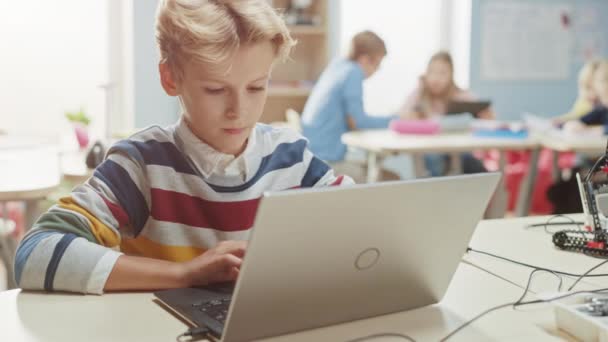 スマートスクールボーイは、ロボット工学クラスのソフトウェアをプログラムするためにラップトップを使用します。才能豊かな子どもたちがテクノロジーを使って働く小学校理科教室 — ストック動画